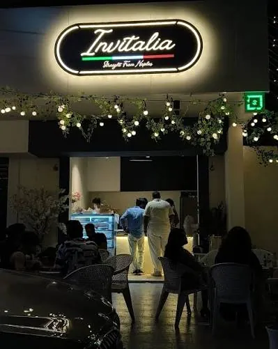 The Invitalia counter seen from the street at night, the lit sign above the door