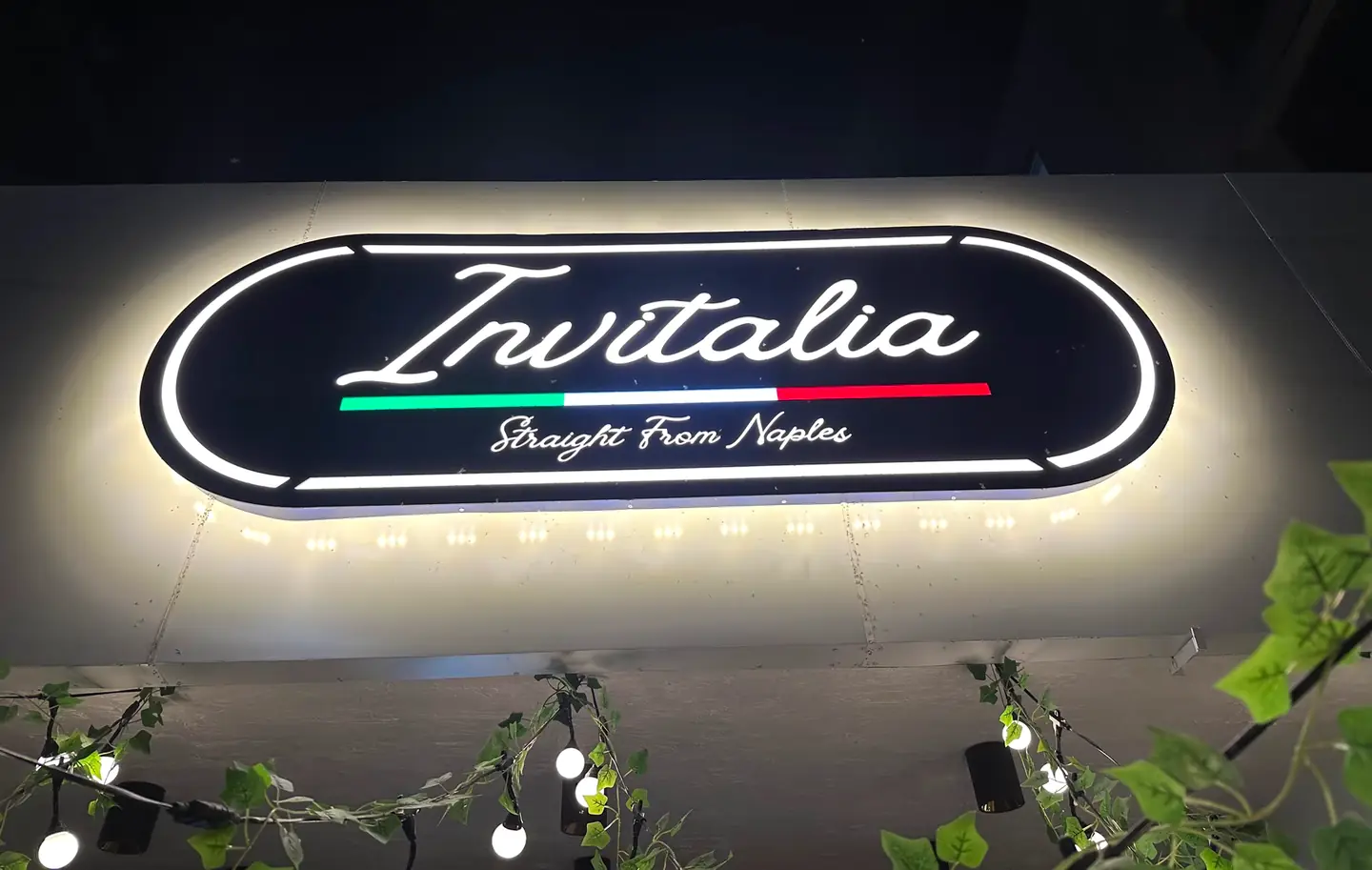 The lit Invitalia sign above the shopfront in Karkardooma, with bulb lights and ivy underneath it